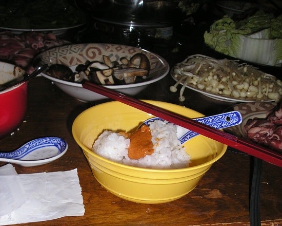 A small bowl with some rice, a yellow sauce, a spoon, and chopsticks.