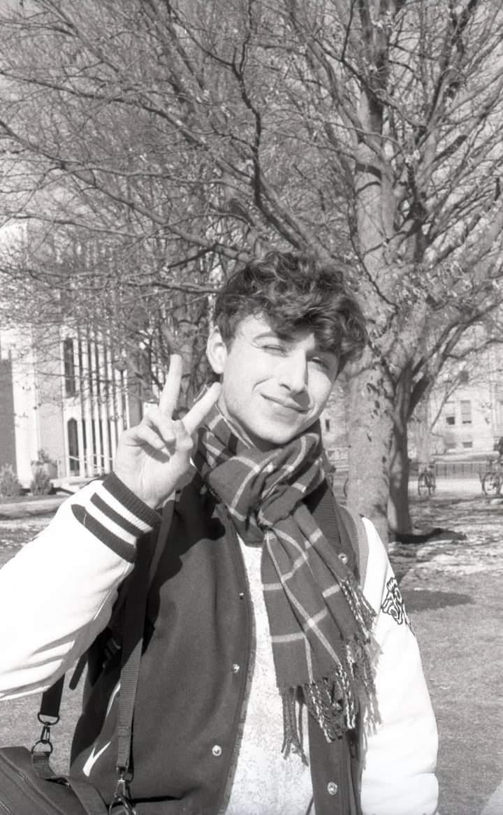Black and white photo of myself smiling in Tappan Square wearing a scarf and university jacket doing a peace sign. 