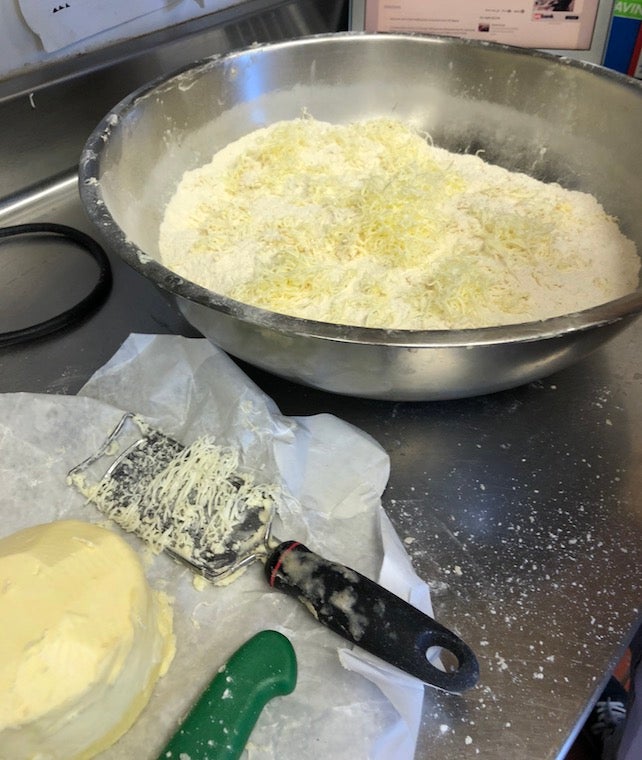 A bowl filled with flour and shreds of butter. A chunk of butter and a fruit zester sit beside it