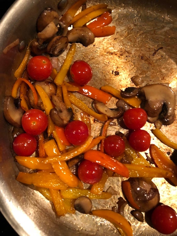 Tomatoes, mushrooms,, and peppers being cooked in a pan