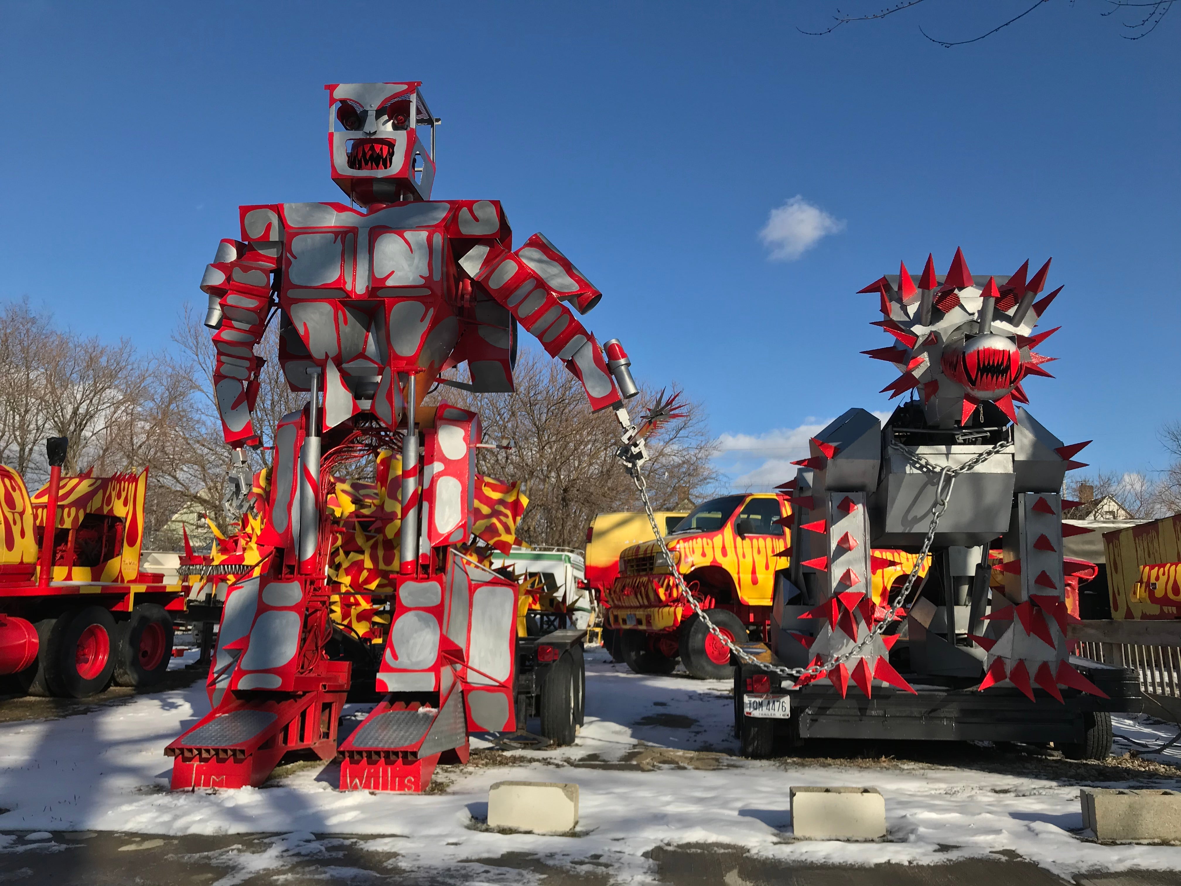 A large grey and red robot and spiked dog with red and yellow trucks in the background