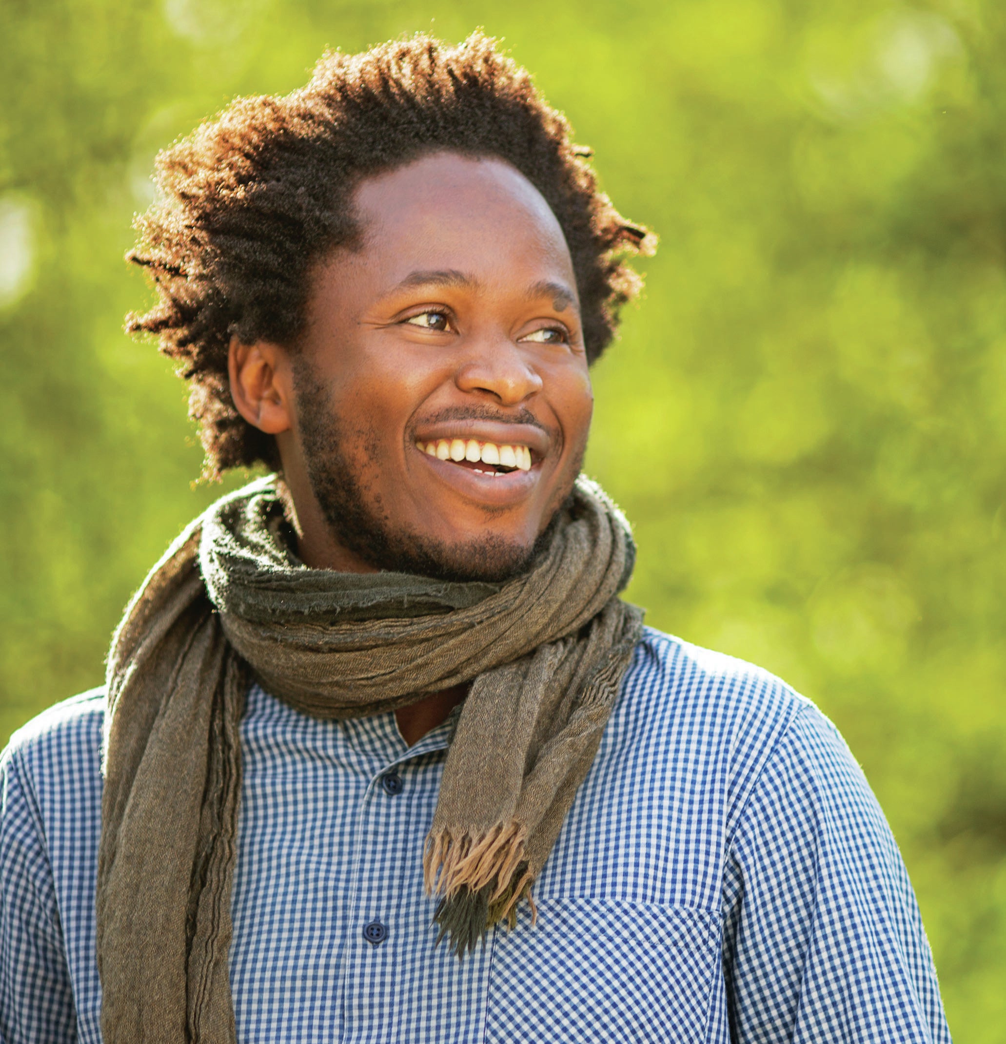 Ishmael Beah outside with a blue shirt and green scarf.