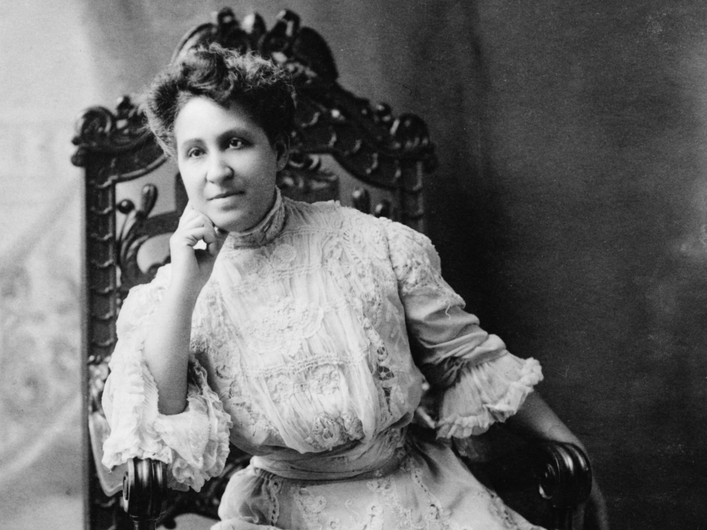 A black and white photo of Mary Church Terrell in a white dress sitting in an intricately carved chair.