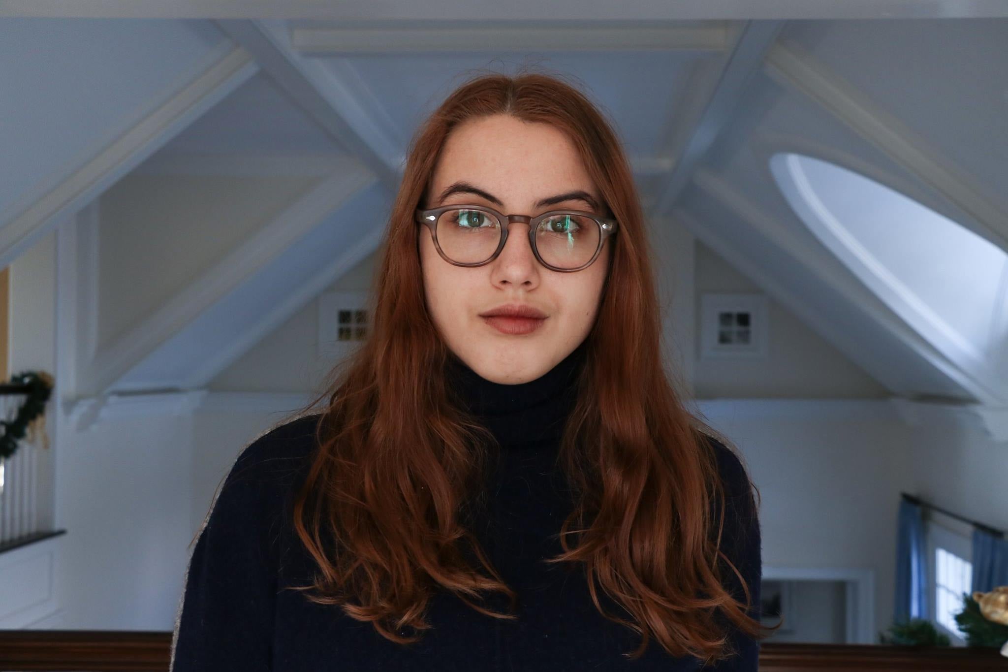 emily with black tortoiseshell glasses, medium-length red-brown hair, and a black turtleneck.