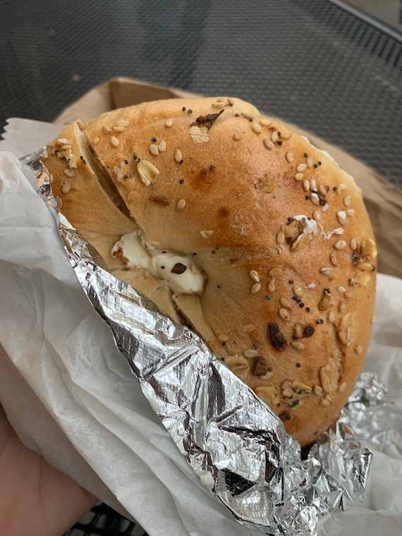 Ilana holds a foil-wrapped everything bagel with cream cheese.