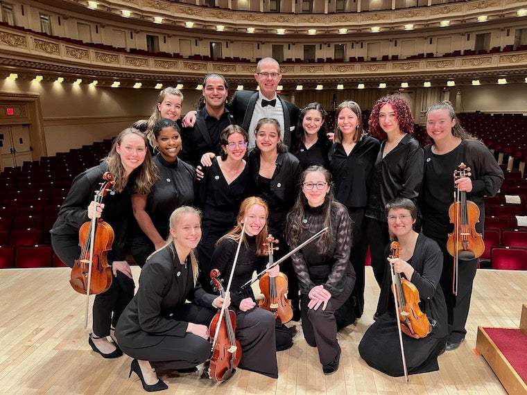 a group of people wearing concert black dress smile on a stage.