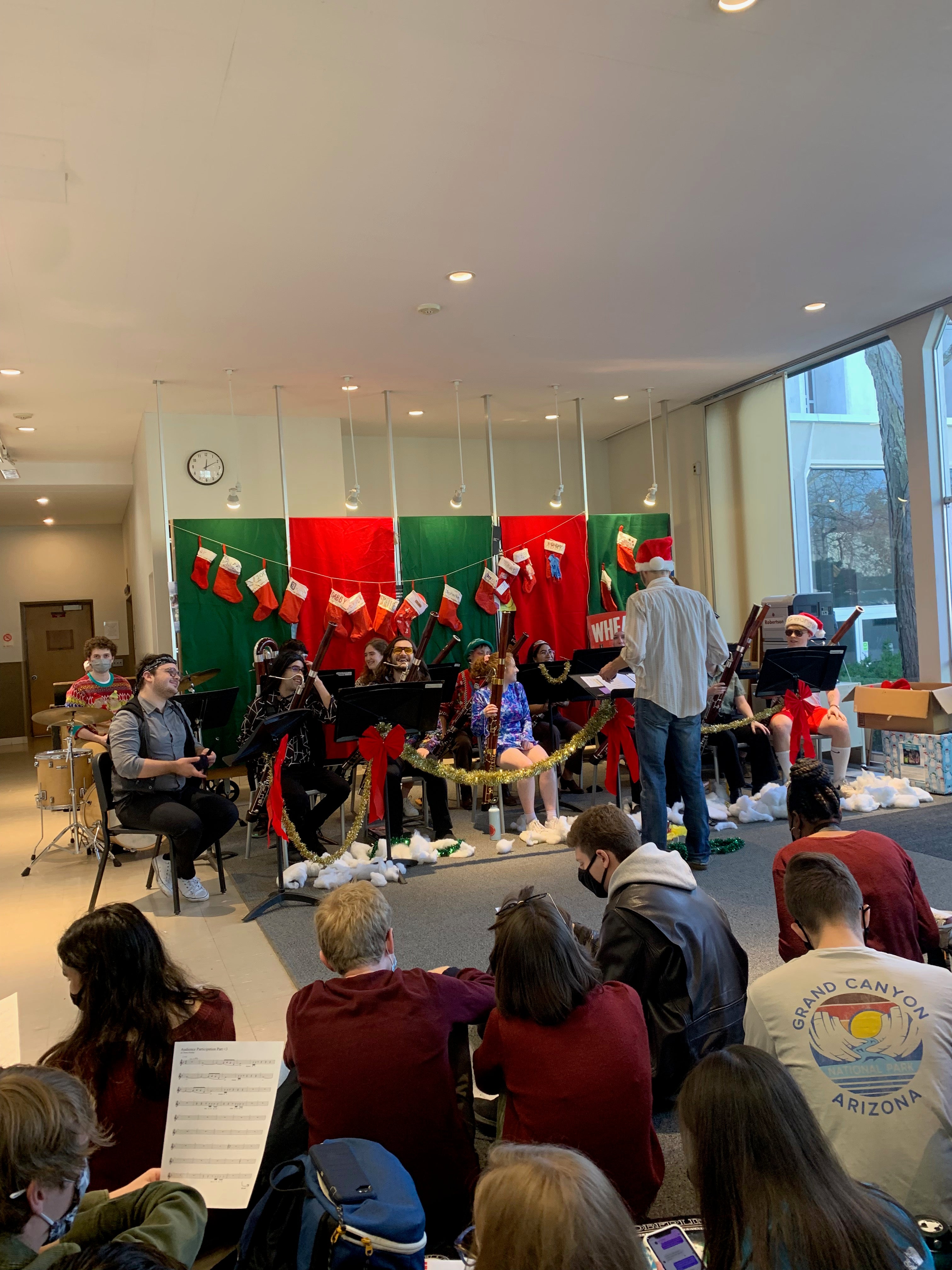 about 12 bassoon players sit and smile in costume in the Conservatory lounge while students on the floor look on