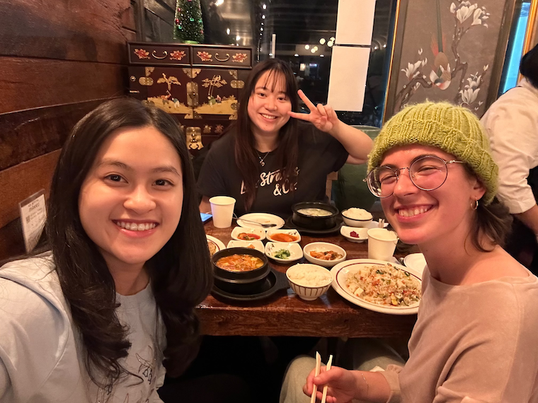 Ilana sits with two other people at a table that has many dishes of food. 