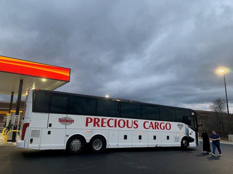 white coach bus with red lettering on the side that says "precious cargo" parked at a gas station. 