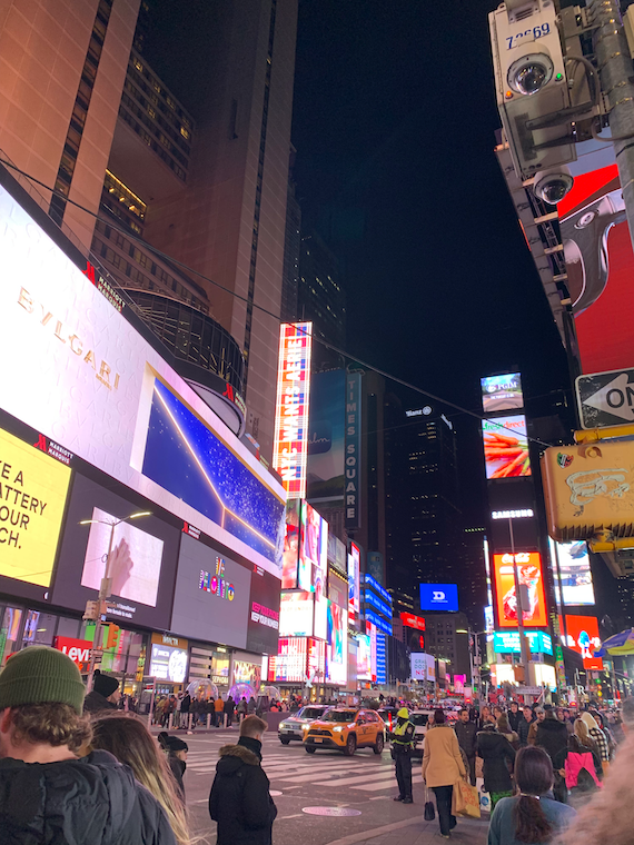 many people walk along a road with flashy billboards all around. 