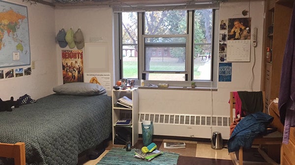 Twin bed by a window looking out on a grassy space. The room looks clean but lived in.