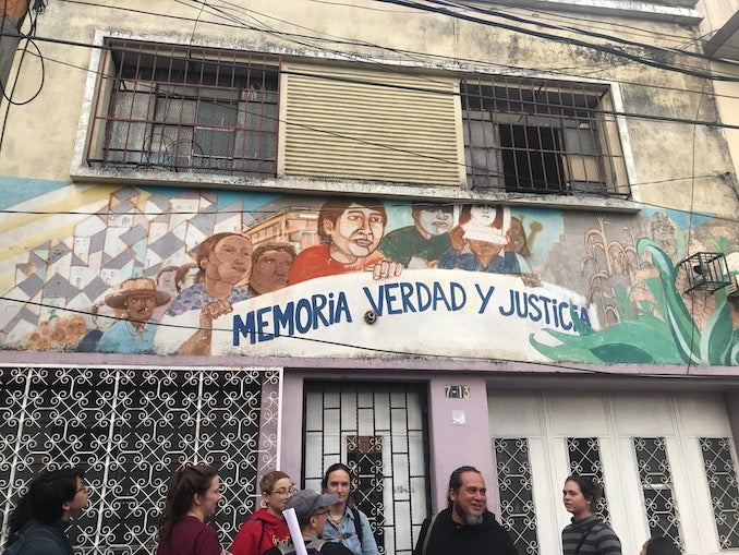 A wall with a mural reading "Memoria, Verdad, Justicia" (memory, truth, justice) and some people standing below.