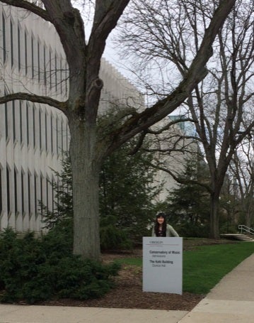 Girl standing behind sign in front of Oberlin Conservatory of Music.