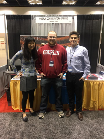 A girl and two guys standing by the Oberlin booth at a convention.