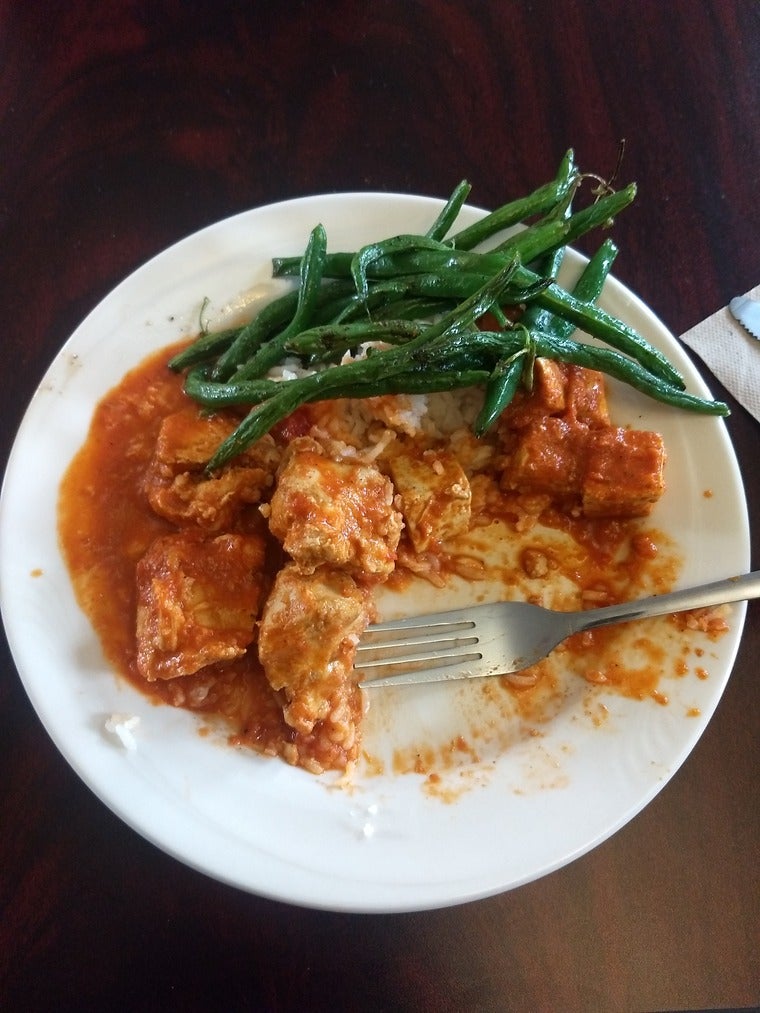 Half-eaten plate of chicken and tofu tikka masala and green beans