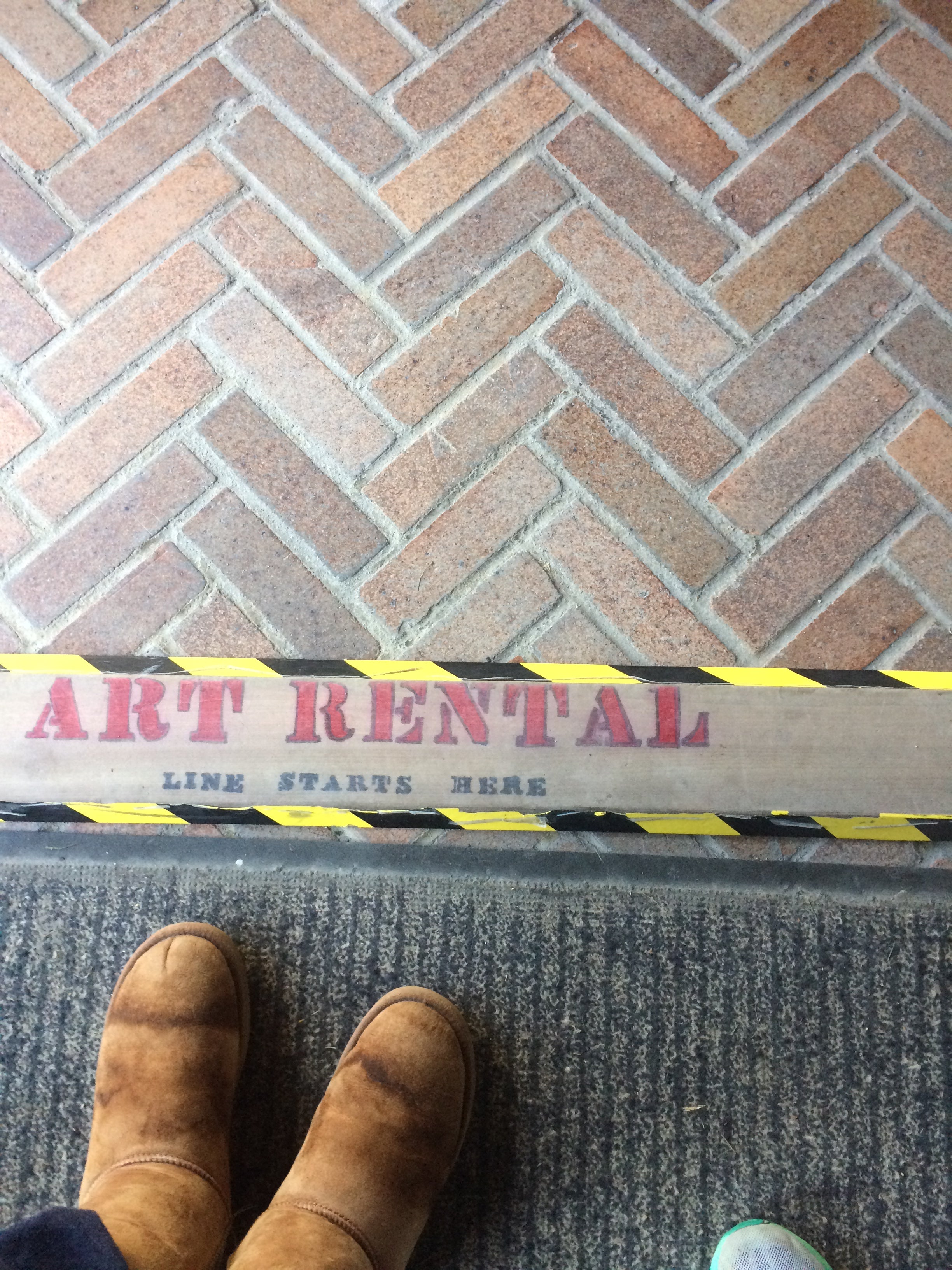 A pair of boots stand on a brick floor with a sign in front of them that says "ART RENTAL"