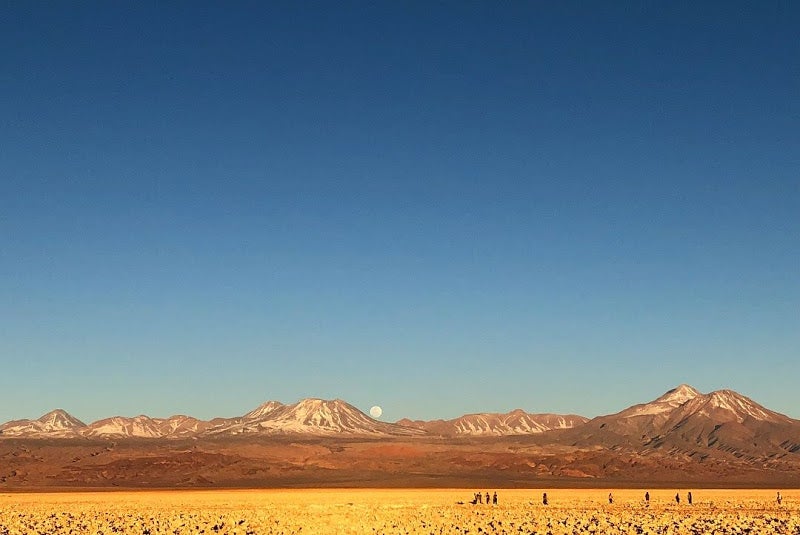 a salt flat in San Pedro de Atacama with the moon rising in the background over a volcano