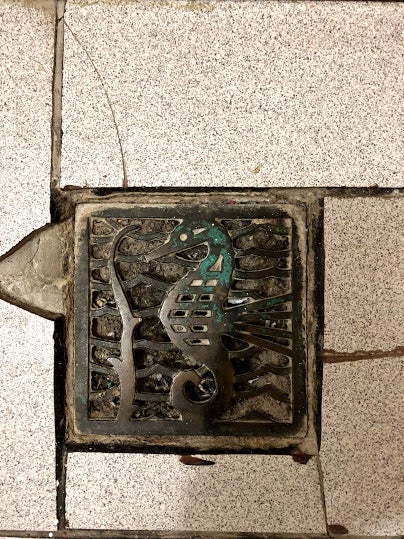 a metal drain in the shape of a seahorse in a tile floor