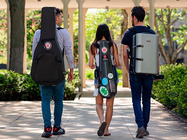 Students with musical instrument cases walk down a campus path.