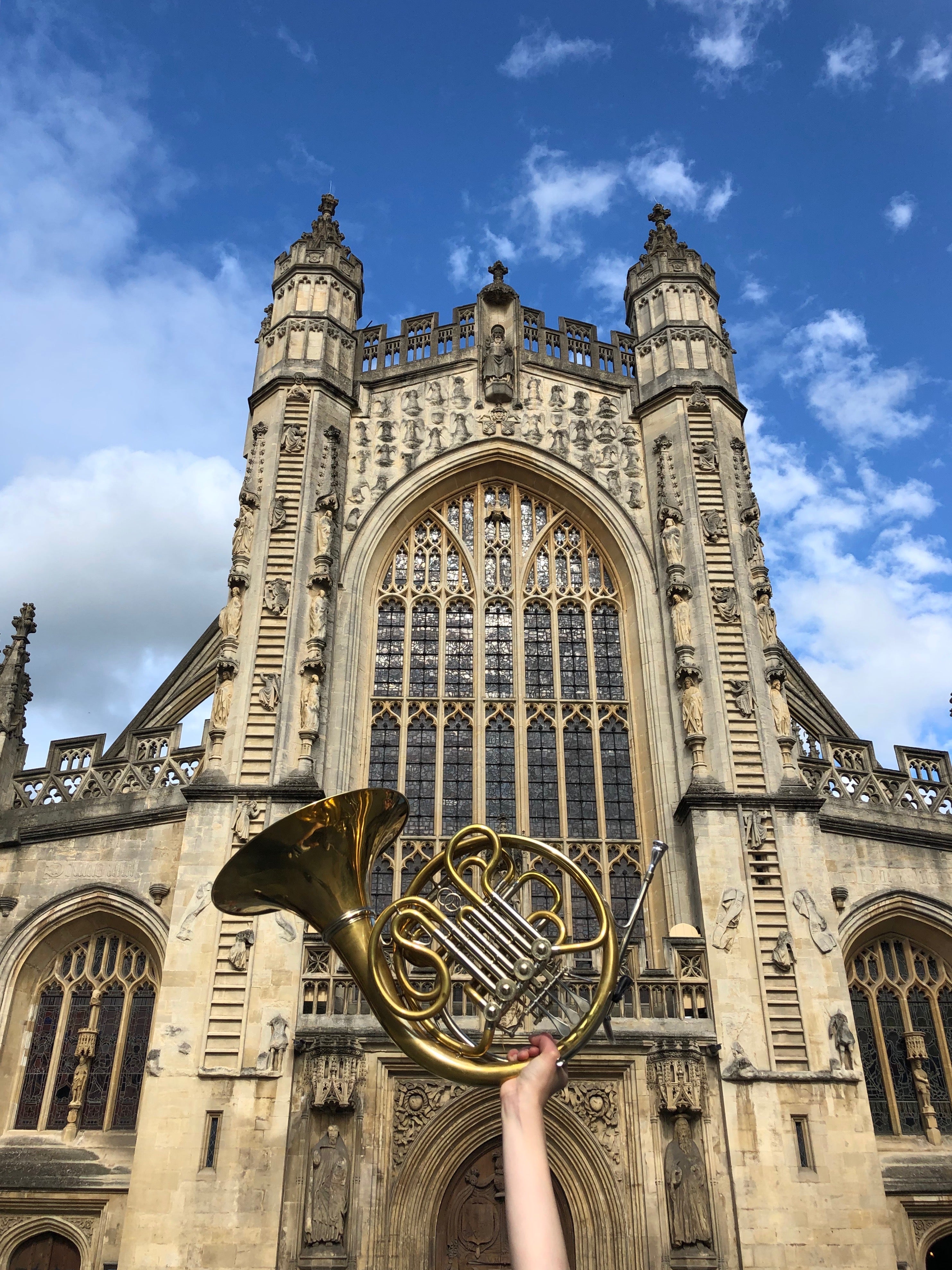  A French horn in front of the abbey. The horn is held up by a person out of the frame.