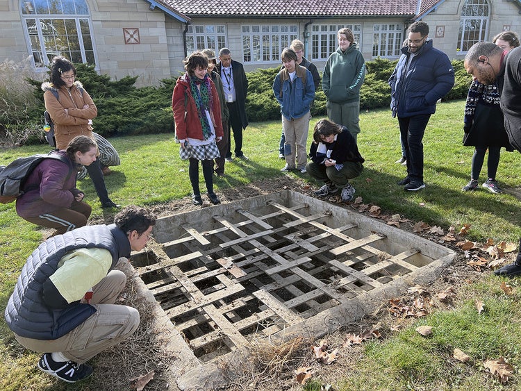 Photo of Fiona Giménez-Collins and students observing the Mary Miss’s 1975 Untitiled installation, a 7’ x 7’ x 2’ pit with layers of wood lattice, carved out from the Allen’s lawn.