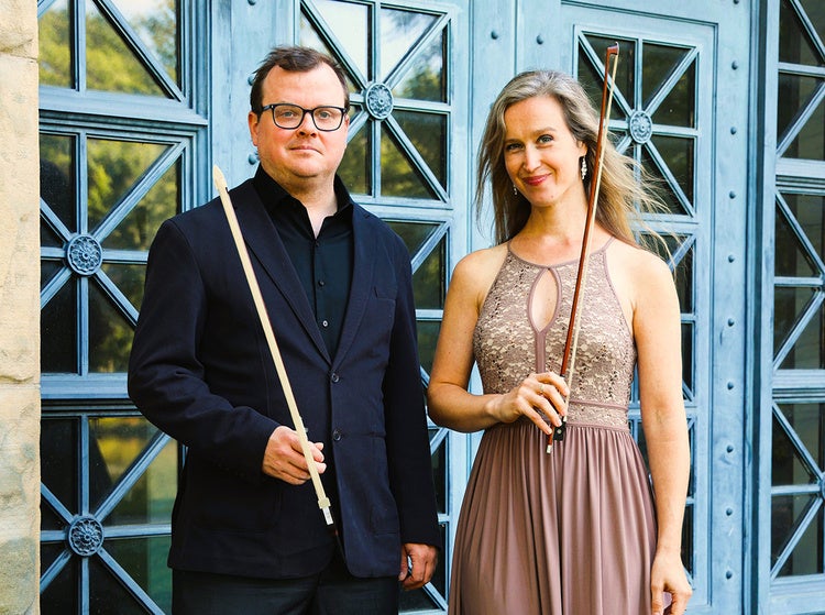The portrait shows two formally dressed musicians standing before an ornate blue-green entrance, each holding a bow.