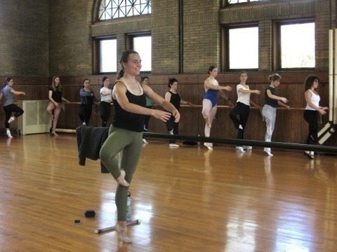 A BalletO board member balances at the barre, demonstrating a combination to beginner students.