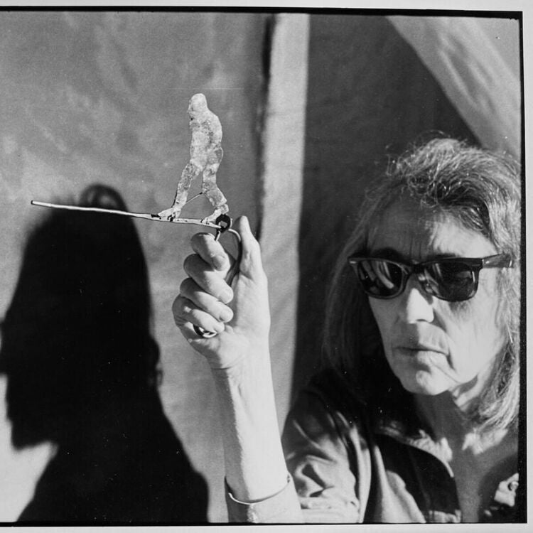 Black and white image of June Leaf holding her kinetic sculpture Woman Walking (1978) while wearing sunglasses. Photo taken by Brian Graham.