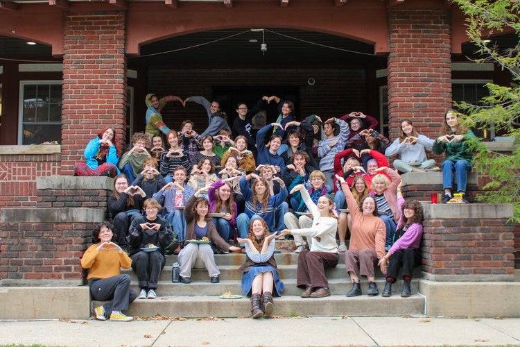 Members of Keep Co-op sitting together on the front steps, making a heart with their arms