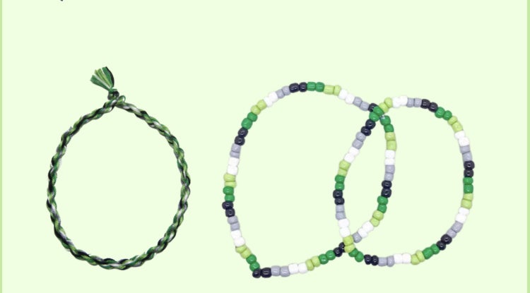 A woven friendship bracelet 2 beaded friendship bracelets, all in the colors of the aromantic flag, on a light green background