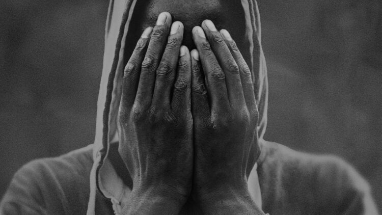 Grayscale photo of a black person covering their face with their hands