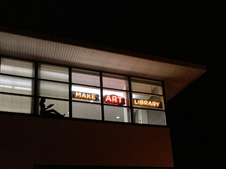 Silhouette of a reader seated in a window, lit from behind by interior lighting