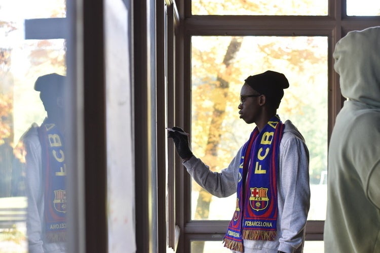A young man writes with a marker on a notepad with fall leaves in the background.