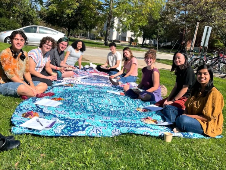 students of all identities sit together on a picnic blanket on the grass of Tappan Square