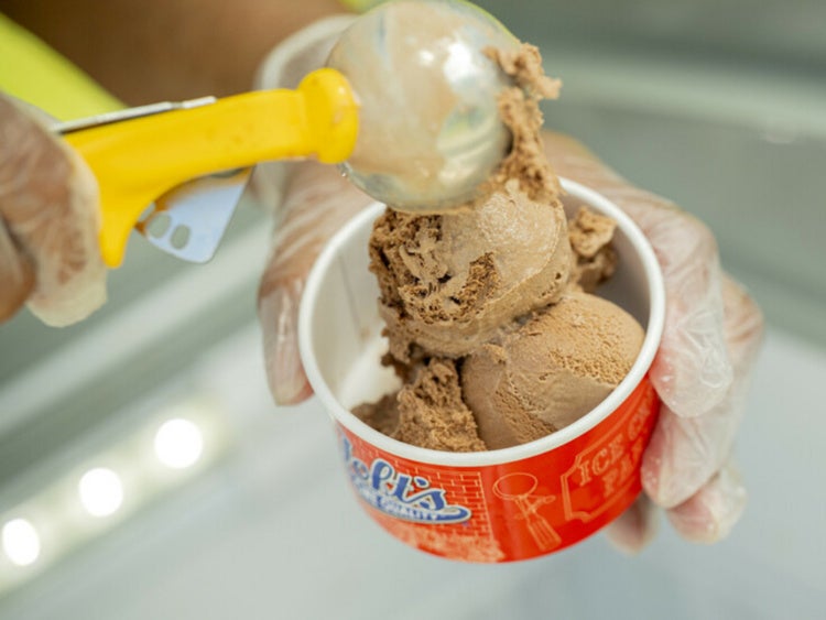 Hands scooping chocolate ice cream into a cup