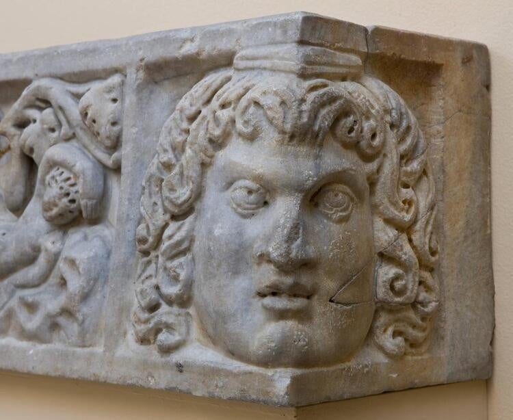 The photo is of the corner of a stone structure that contains a face with long curly hair.