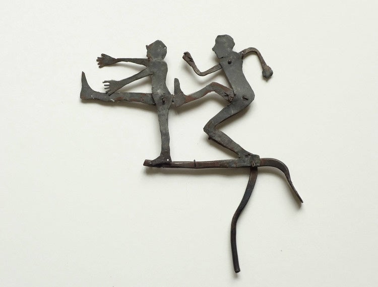 Photograph of June Leaf's kinetic sculpture The Kick. The sculpture features two figures, one on the right side in a kicking pose, and the other, on the left, reacting to being kicked.