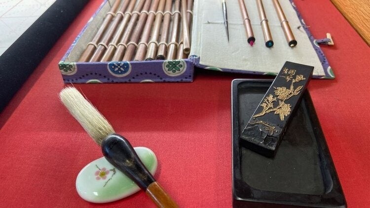 Calligraphy set with brush, ink stick, ink stone, and colored pens on a red surface.
