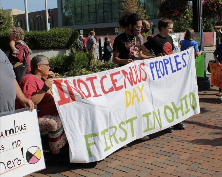 People holding a banner that reads ‘Indigenous Peoples’ Day First in Ohio’ at a public gathering.