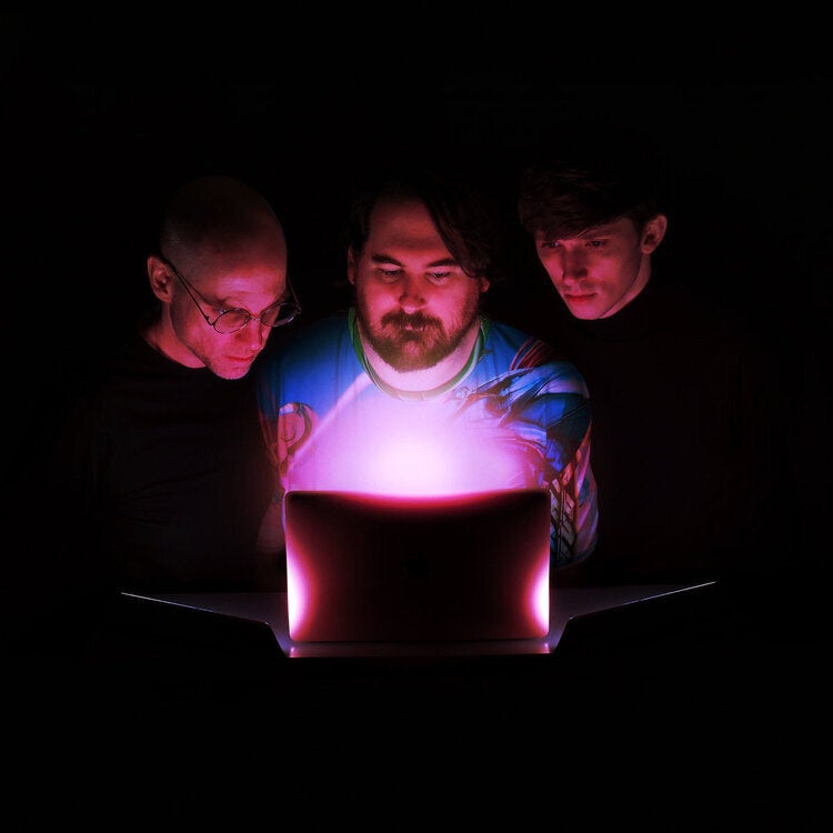 Members of the group Death's Dynamic Shroud looking at an illuminated screen in a dark room
