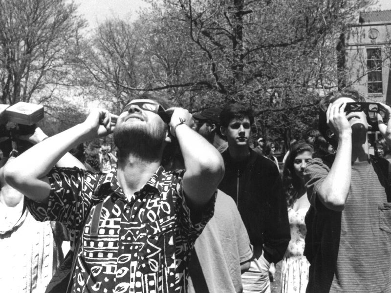A crowd of students outdoors, looking at the sky wearing eclipse glasses. (Black and white archival photo.)