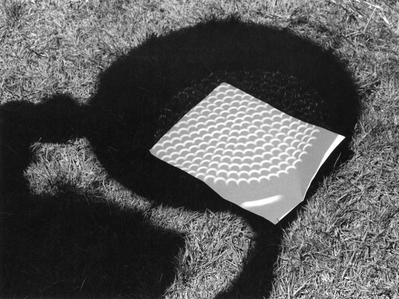 Black and white photo of eclipse shadow shining through colander onto paper