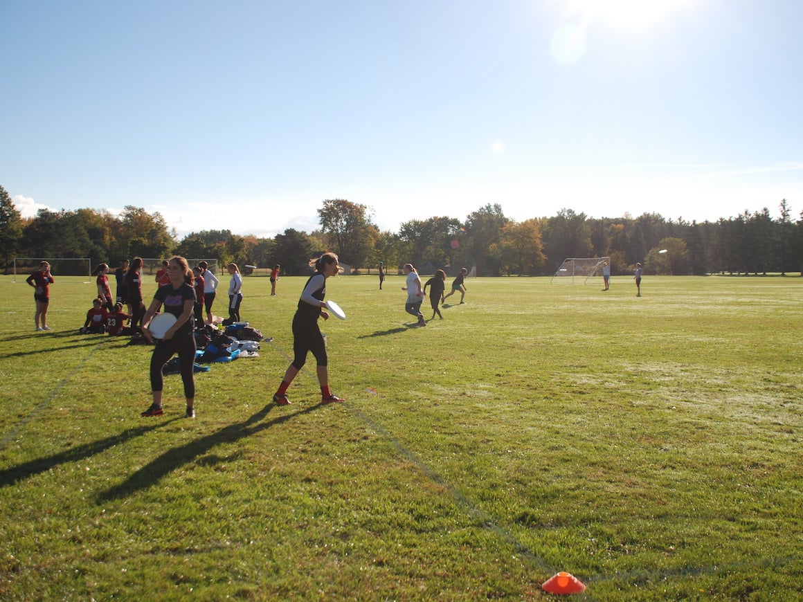 group of young women gathered on large open grassy field playing frisbee