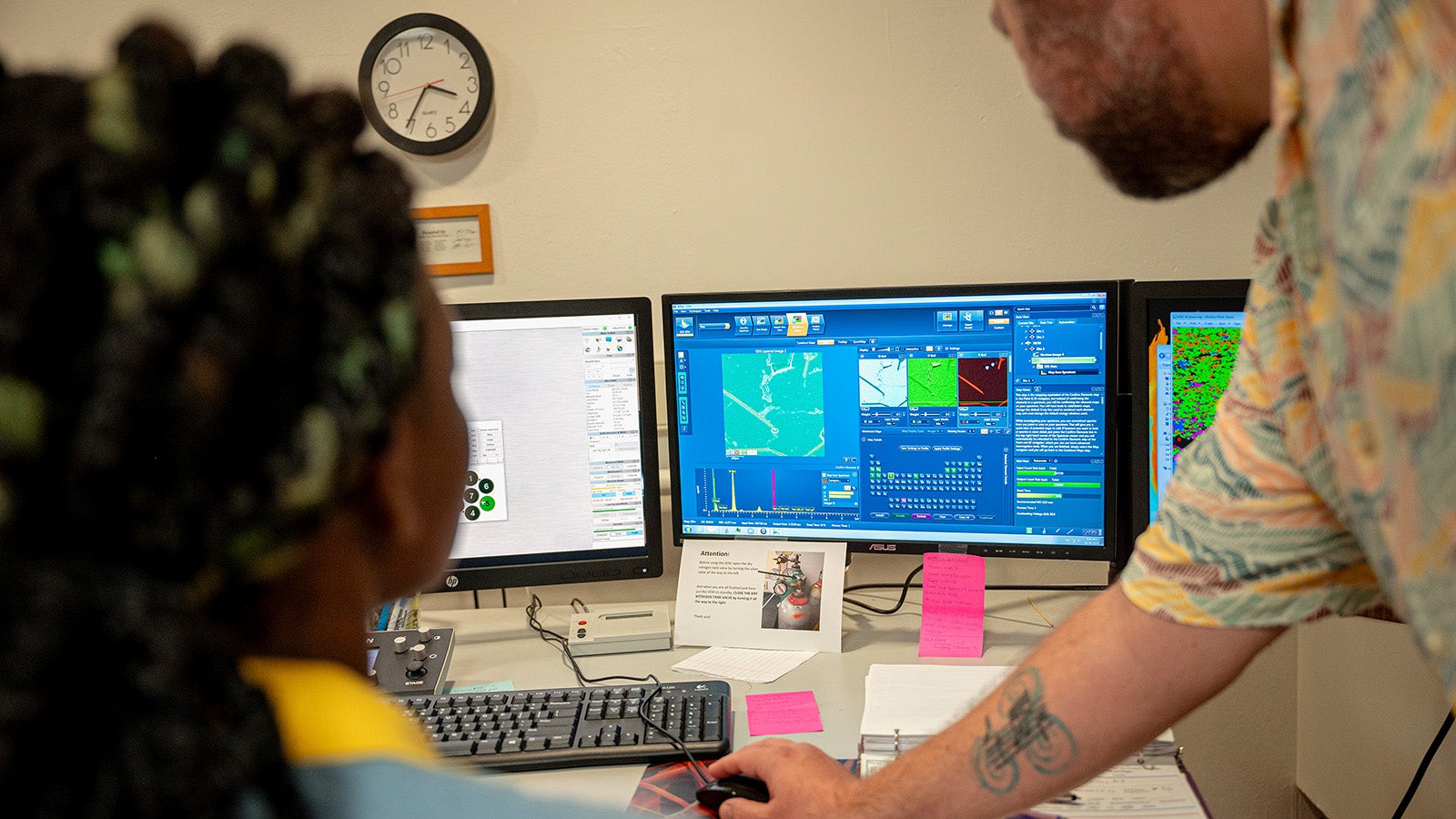 A professor and student work at a computer screen showing detailed graphs of data.