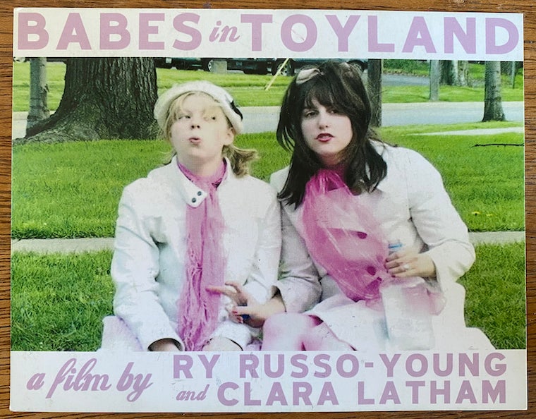 Two female students in white outfits with pink scarfs sitting on the grass