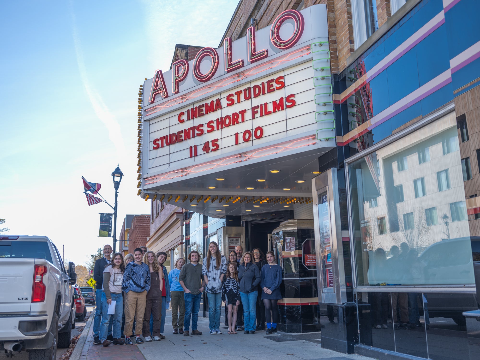 A group of people standing under the movie theater Apollo marquis and smiling for the camera