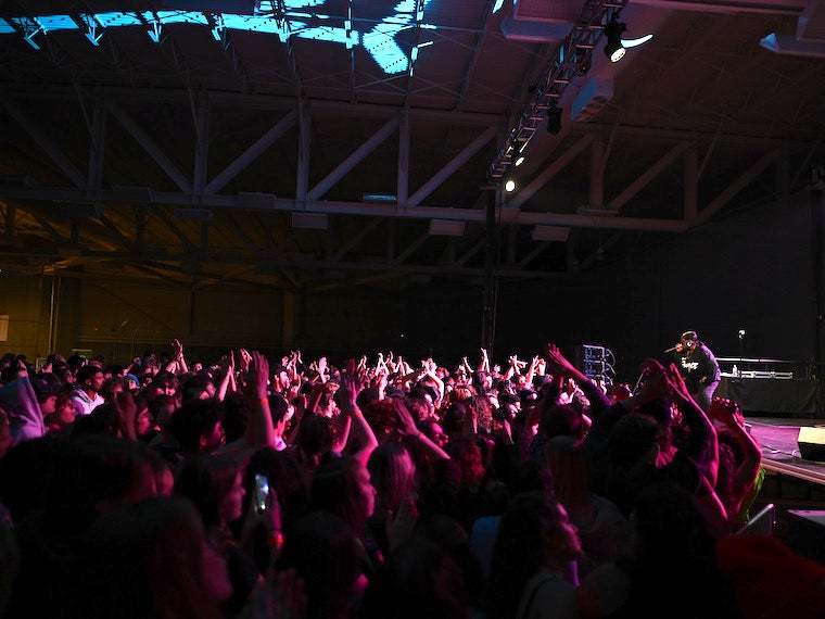 A large group of students dance to a rapper at a concert.