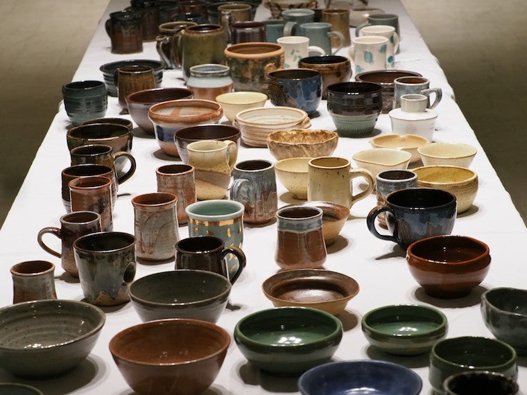 A long table filled with handmade mugs and bowls.