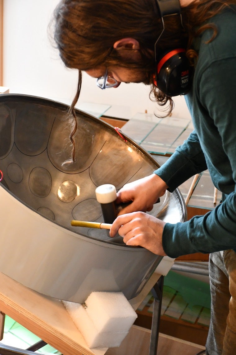 Noah Sanderson working on a steel drum with a hammer. Photo.