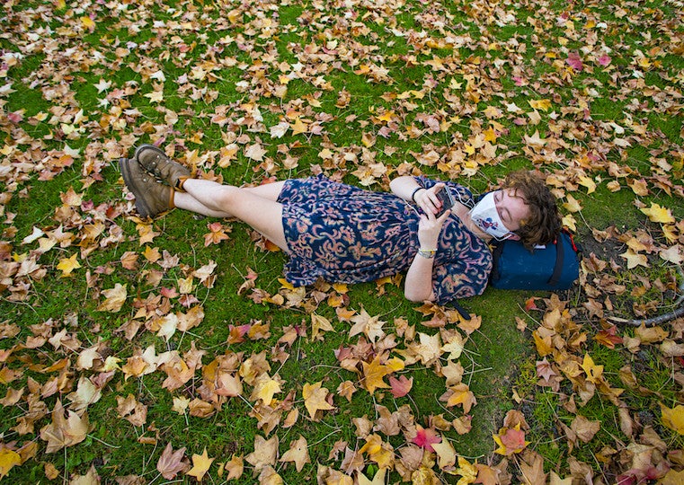 A student lays in the grass surrounded by fall leaves.